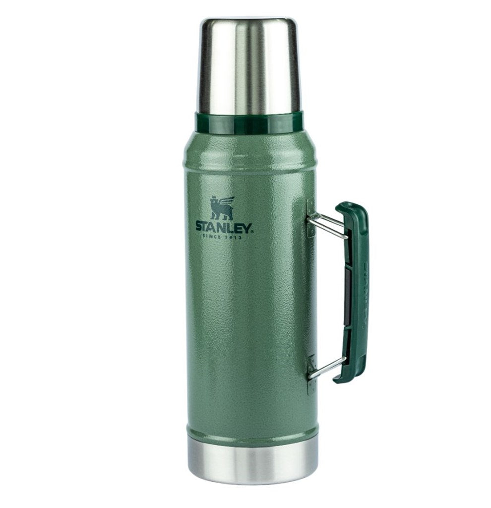 Garrafa térmica verde da marca Stanley. A garrafa tem um design clássico e robusto, com uma tampa de aço inoxidável que também pode ser usada como copo. Possui uma alça lateral verde escura para facilitar o transporte. No corpo da garrafa, está o logotipo da Stanley em preto, acompanhado do texto "SINCE 1913". A base e a parte superior da garrafa são de aço inoxidável.