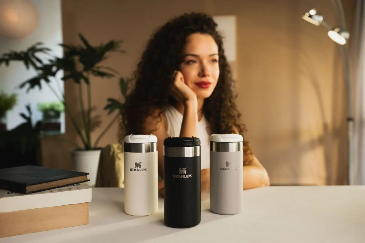 Uma mulher sentada atrás de três das opções de Aerolight Stanley que fazem parte do dia a dia dela.