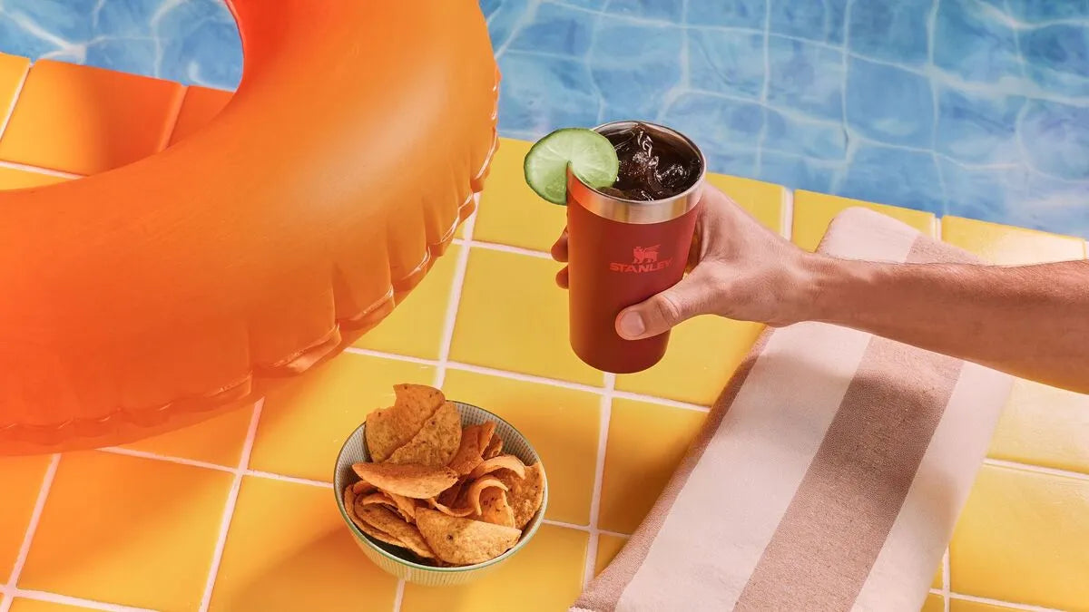 Uma pessoa segurando o copo Stanley na beirada da piscina durante o verão.
