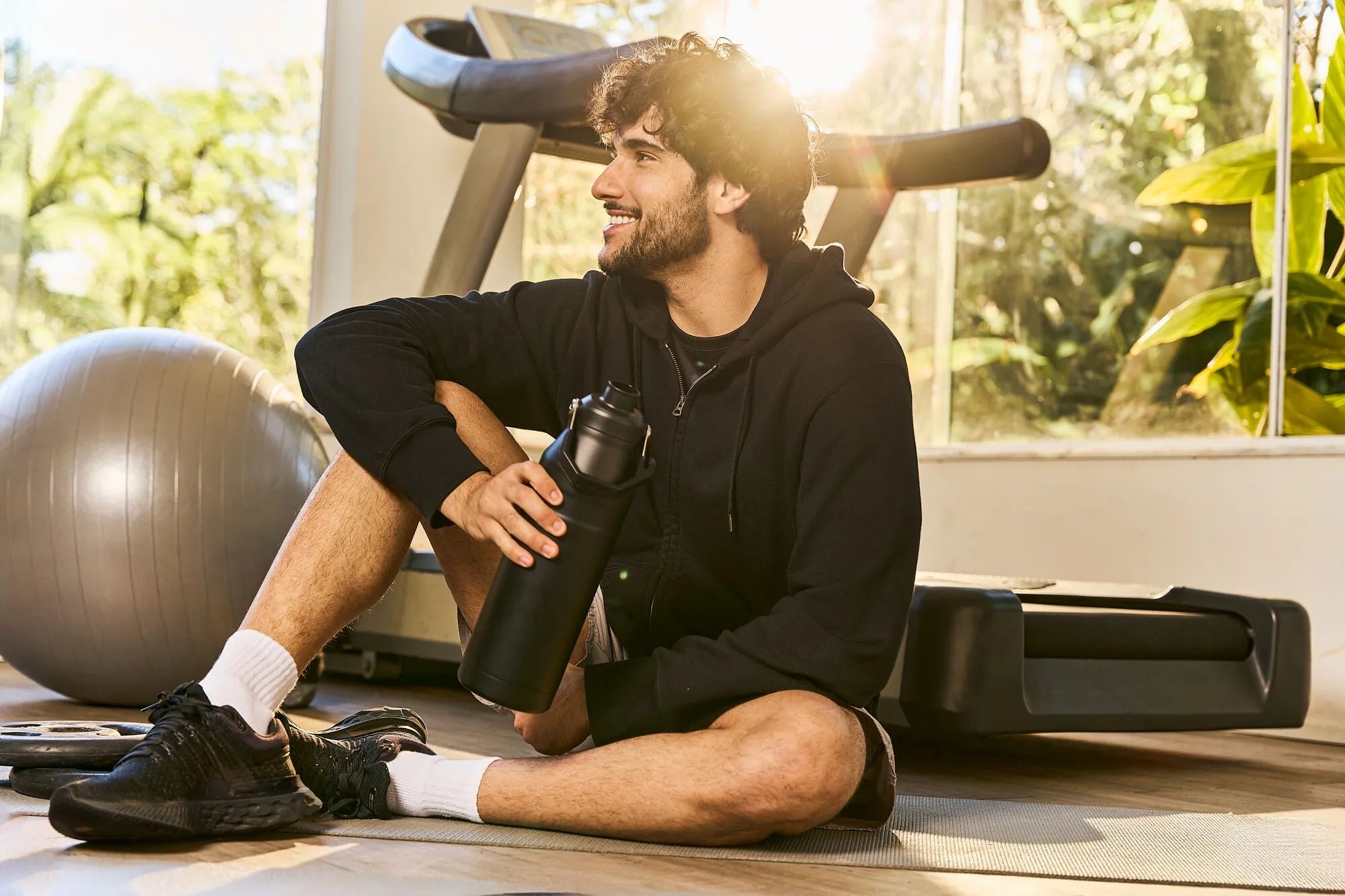 Um homem sentado no chão e bebendo água com uma garrafa da linha Aerolight.