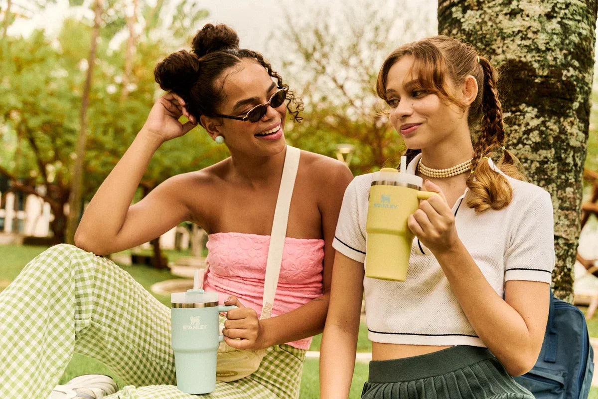 Duas amigas sentadas lado a lado, cada uma segurando o seu Mini Quencher Stanley 1913.