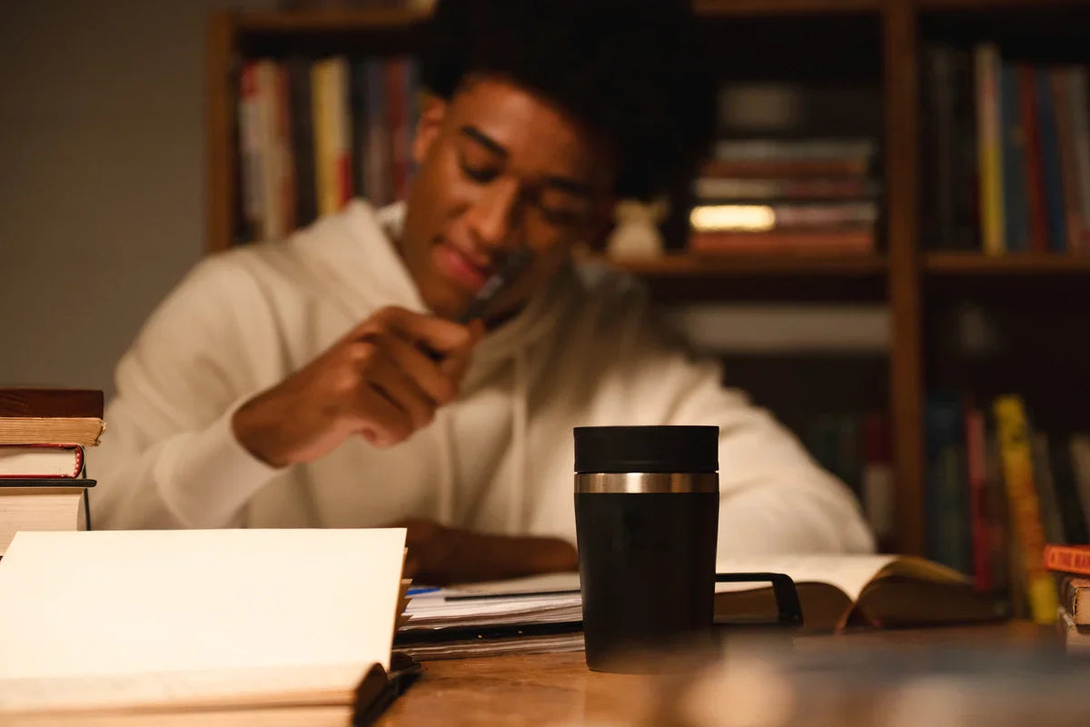 Uma pessoa sentada na mesa estudando com a Mug Térmica Café To Go Stanley ao lado para pausas estratégicas com a bebida favorita.